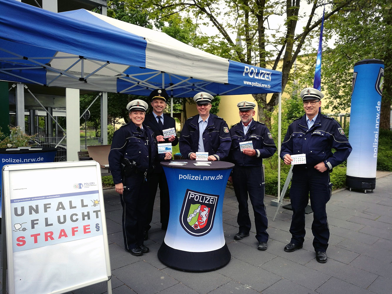 Fünf Polizeibeamte am Aktionsstand halten Postkarten in die Kamera.