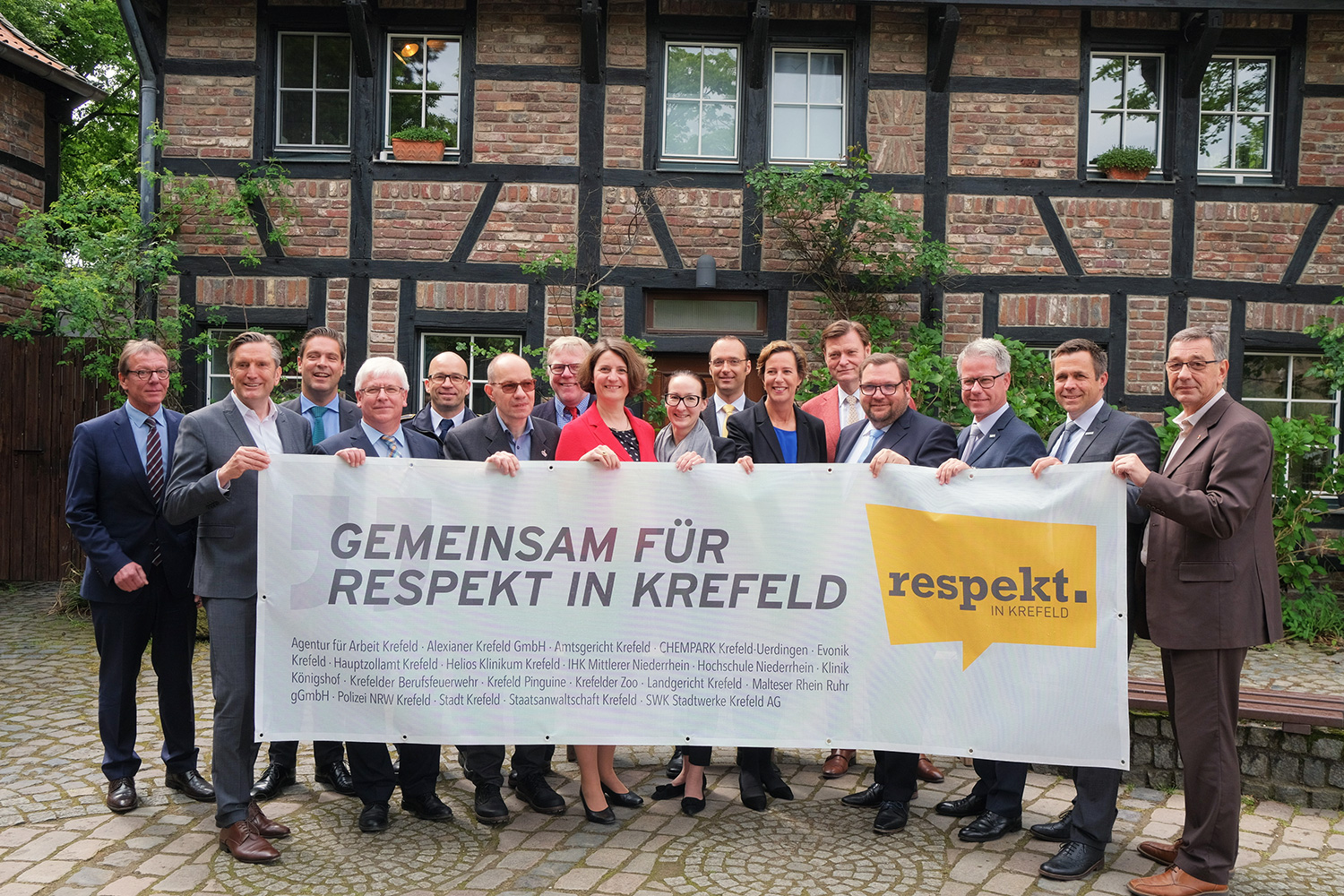 Die Leiterinnen und Leiter aller mitwirkenden Institutionen halten ein Banner mit der Aufschrift: Gemeinsam für Respekt in Krefeld. Ein Fachwerkhaus (Zooscheune) befindet sich im Hintergrund.