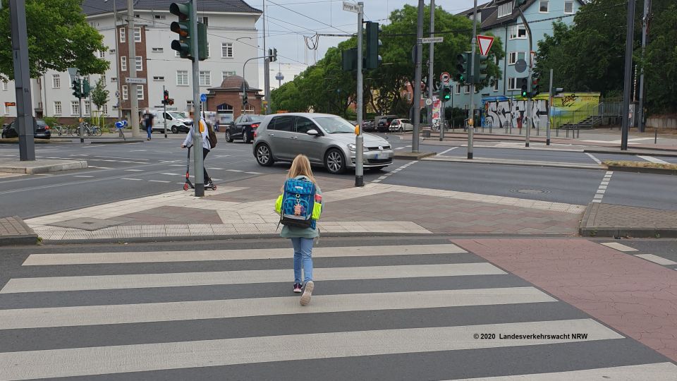 Kind mit Schulranzen überquert einen Zebrastreifen.