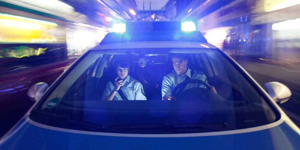 Frontansicht Streifenwagen. Zwei Beamte im Wagen. Blaulicht leuchtet.