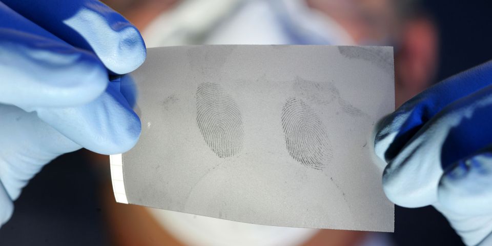 Kriminalbeamter hält eine Folie mit Fingerabdrücken